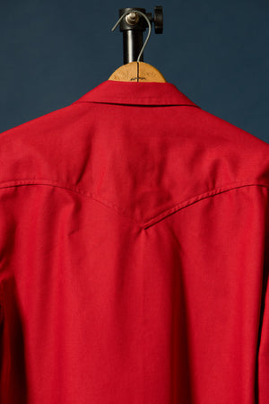 A bright red western-style shirt jacket displayed on a wooden hanger against a dark navy blue background.