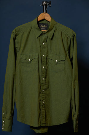 An olive green long-sleeve button-up shirt with two chest flap pockets, hanging on a wooden hanger against a dark blue background.