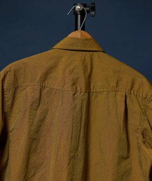 A close-up of the back of a wrinkled brown collared shirt jacket hanging on a black hanger against a dark navy background.