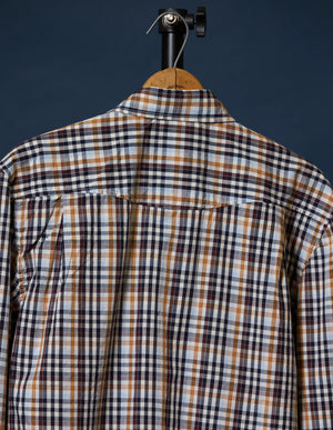 A long-sleeve plaid button-up shirt shown from the back, hanging on a wooden hanger with a black stand against a dark navy background.