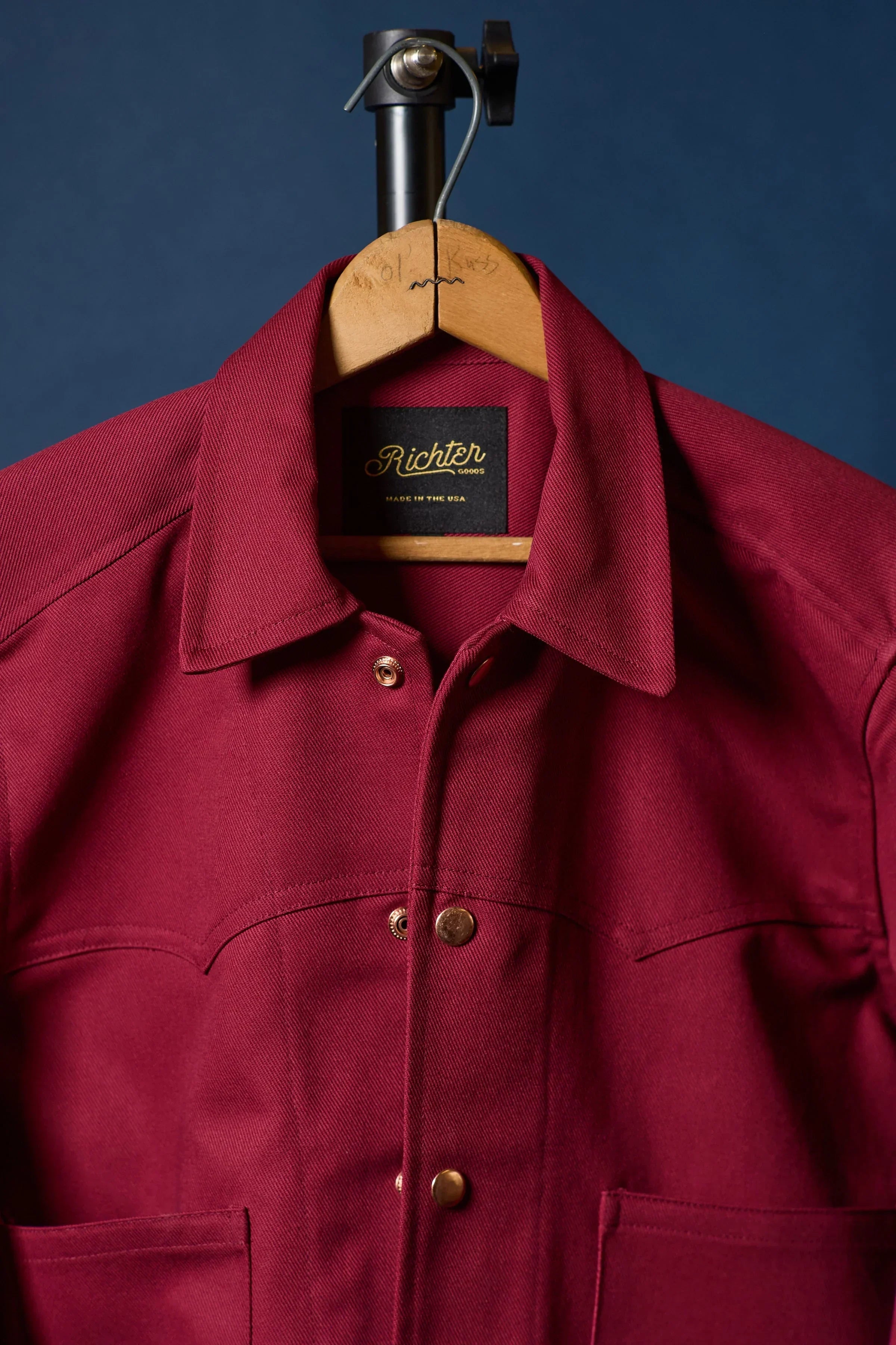 Rhubarb Red jacket on a hanger with 'Richter' label against a blue background