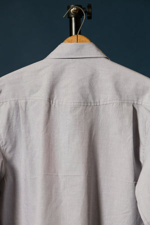 Close-up of the back of a beige long-sleeve button-up duck canvas shirt hanging on a wooden hanger against a dark blue background.