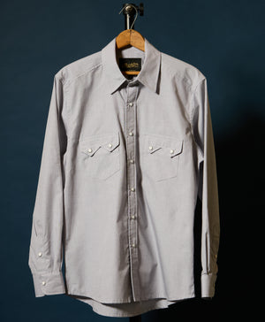 A Beige long-sleeve button-up shirt with two chest flap pockets, hanging on a wooden hanger against a dark blue background.