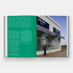 ac5d4c28d0ec1a3a68917c5b4e4dfad0b04142af982ba0d6278e62549173c69e, open book showing Prada Marfa art installation and a person in cowboy hat, front view