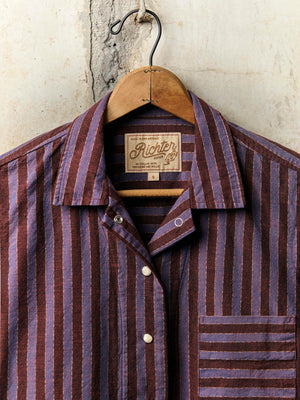 Striped shirt on a hanger with a visible brand label against a textured wall.