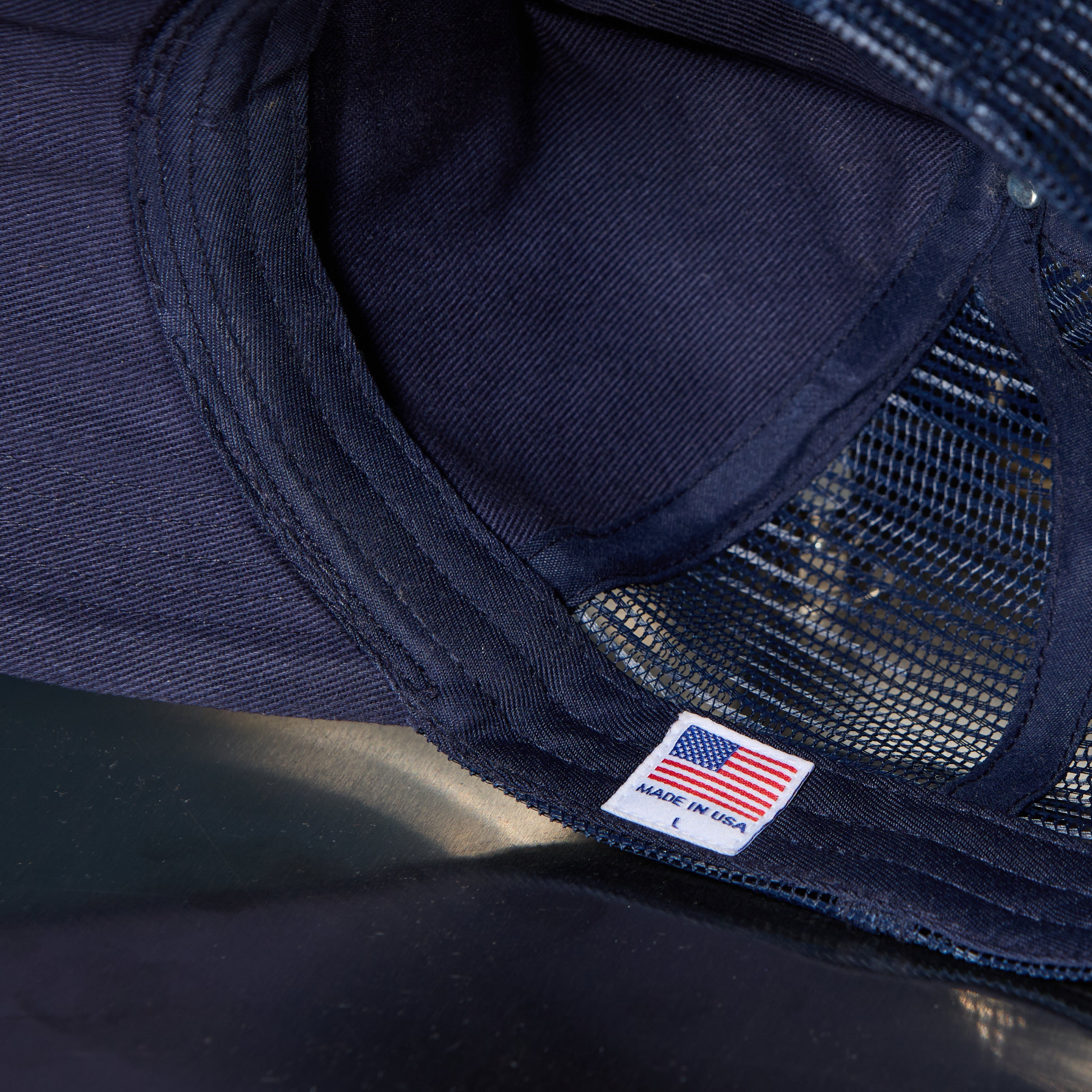 Close-up of a dark navy trucker hat showing the mesh back, stitched fabric edge, and a small white 'MADE IN USA' patch with an American flag.