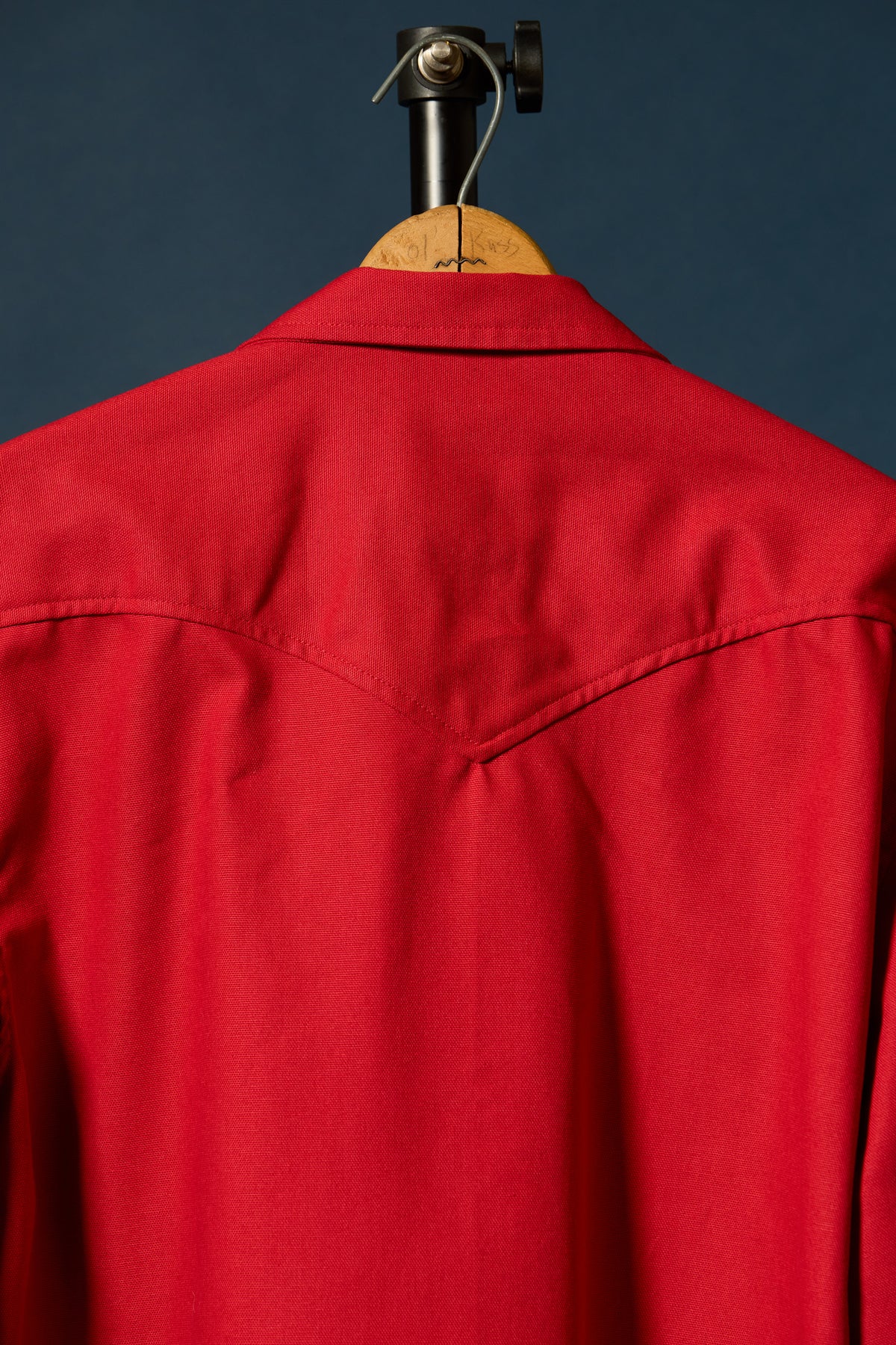 A bright red western-style shirt jacket displayed on a wooden hanger against a dark navy blue background.