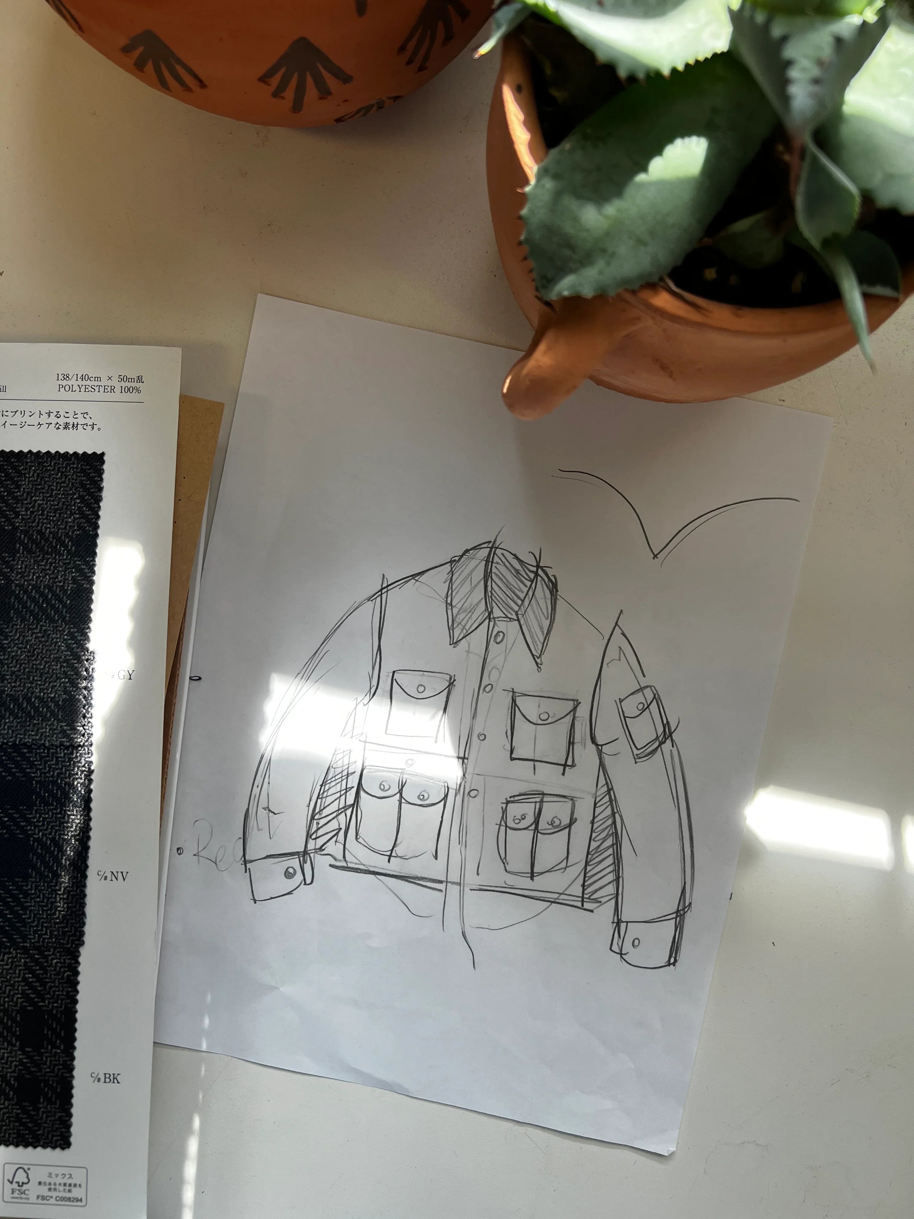 Jacket design front sketch on paper with fabric swatch and potted plant