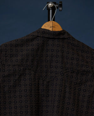 A dark patterned shirt displayed on a wooden hanger against a dark blue background.