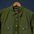 An olive green long-sleeve button-up shirt by Richter, hanging on a wooden hanger against a dark navy blue background.
