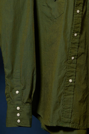 Close-up of an olive green long-sleeve button-up shirt showing the chest pocket, front button placket, and buttoned cuff on the left sleeve against a dark blue background.