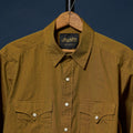 A close-up of a brown textured button-down shirt hanging on a wooden hanger against a dark navy background. The shirt features two buttoned chest pockets and a visible 'Richter Goods' 
label.