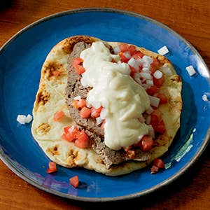 Plated dish with meat, tomatoes, and white sauce on a blue plate