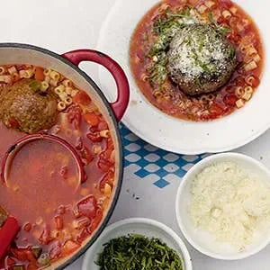 Pasta with meatballs, a bowl of soup, and a plate of pasta with a meatball on a blue and white checkered tablecloth.