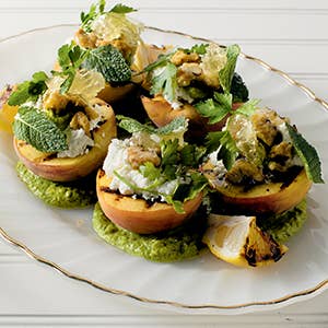 Plated dish of stuffed peaches with pesto and greens on a white plate.