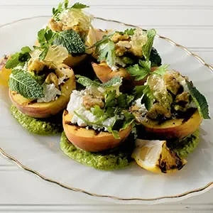 Plated dish of stuffed peaches with pesto and greens on a white plate.