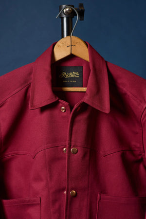 Rhubarb Red jacket on a hanger with 'Richter' label against a blue background