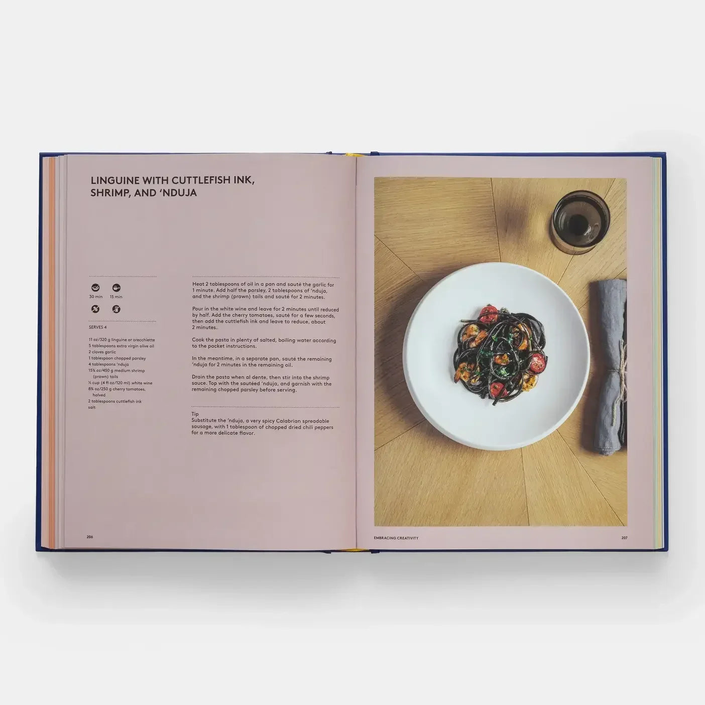 Open book showing a recipe for linguine with cuttlefish ink, shrimp, and nduja on a wooden surface.