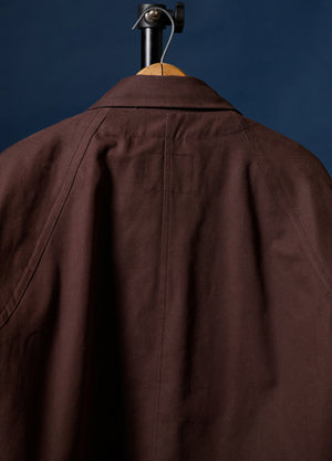 A dark brown jacket or overshirt displayed on a wooden hanger against a dark blue background, showing the back collar and upper back panel.