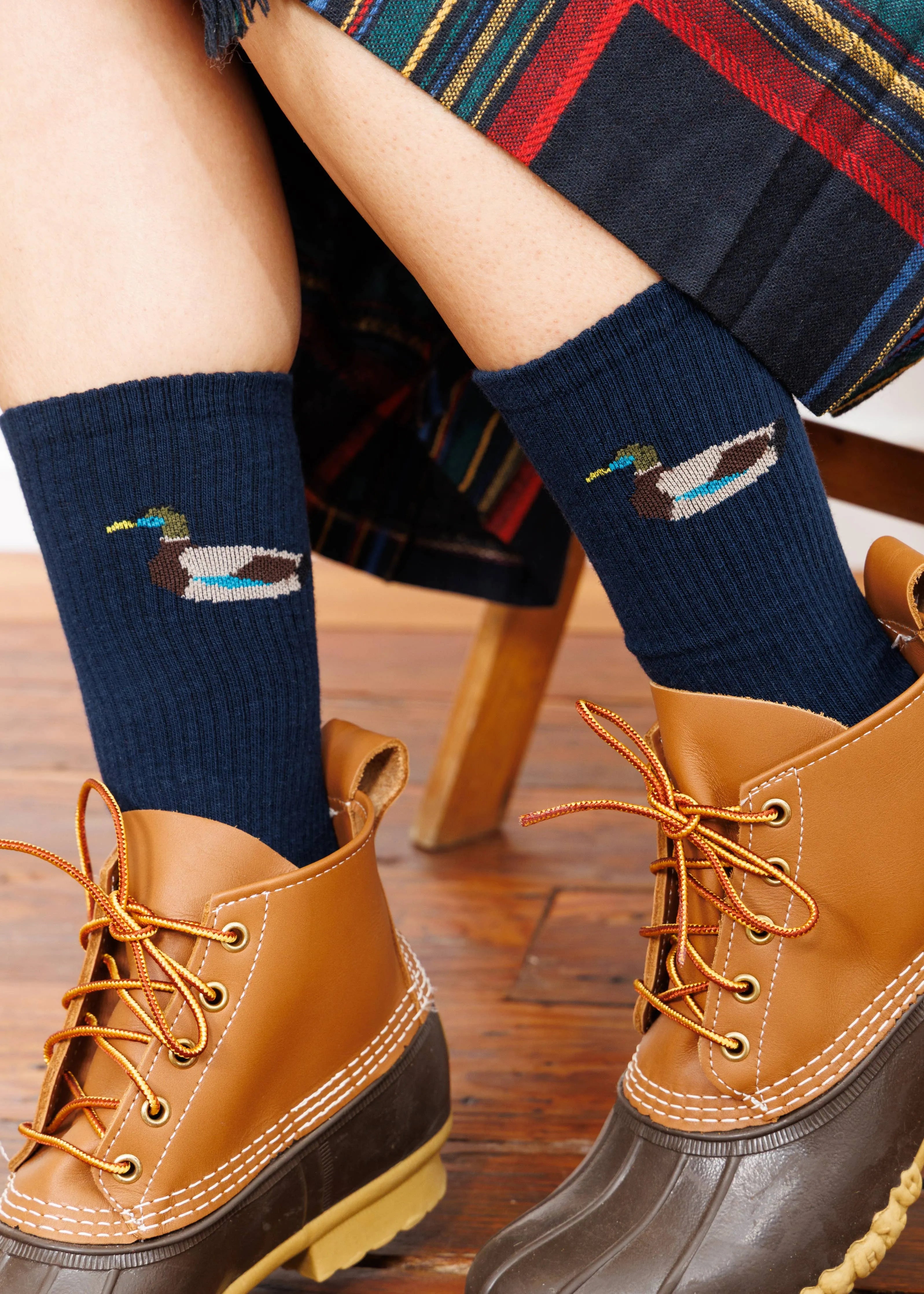 Navy socks with duck design worn with brown boots on a wooden floor.