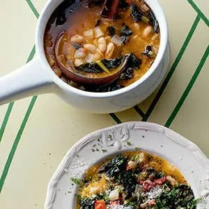 Two bowls of soup with vegetables on a green and white striped tablecloth