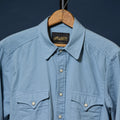 A light blue long-sleeve button-up shirt with two chest pockets, hanging on a wooden hanger against a dark navy background. The brand label inside the collar reads 'Richter'.