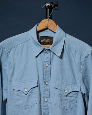 A light blue long-sleeve button-up shirt with two chest pockets, hanging on a wooden hanger against a dark navy background. The brand label inside the collar reads 'Richter'.